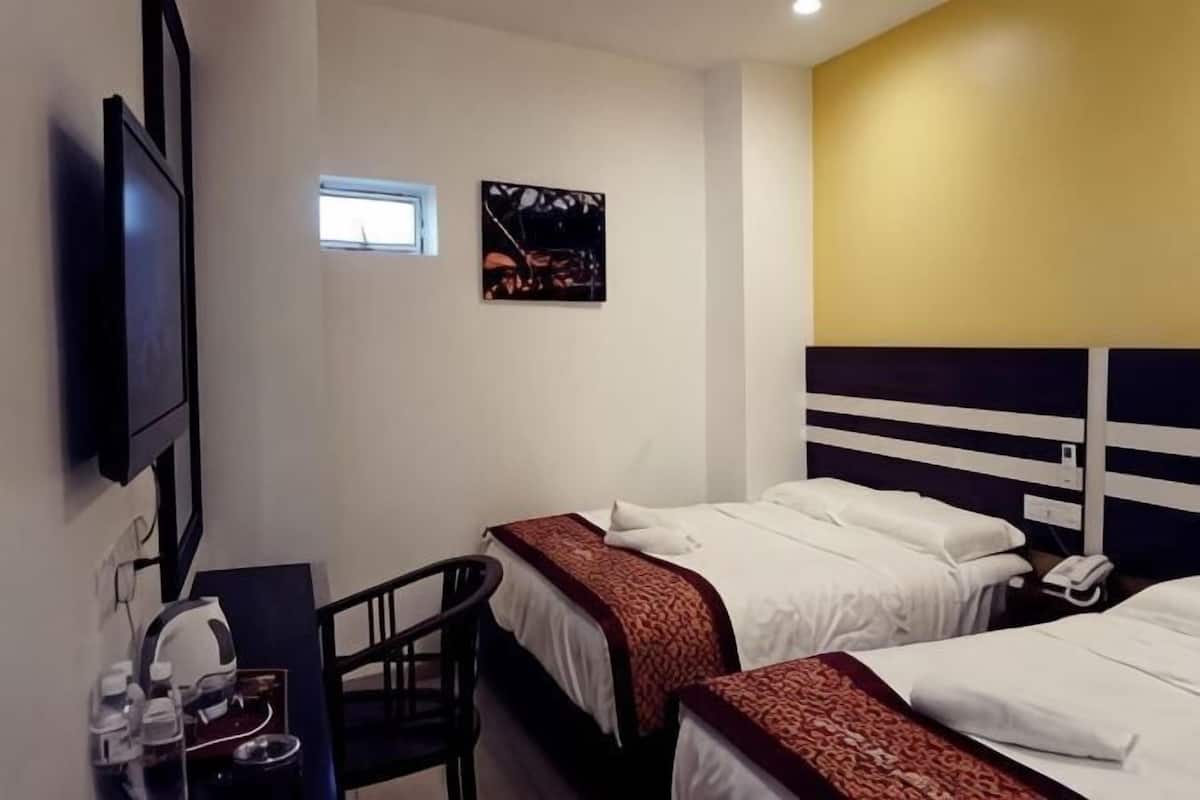 A hotel room with two beds, a desk with a chair, a television, and a small window.