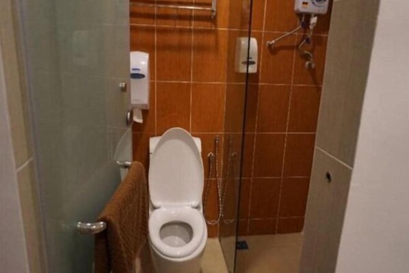 A bathroom with a toilet, a hand dryer, and a shower area.