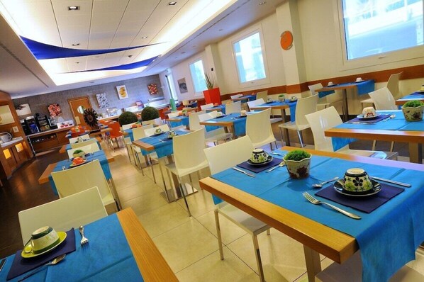 Un comedor moderno con mesas dispuestas para comer, con manteles azules y sillas blancas.