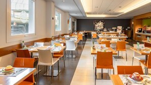 A spacious dining area with multiple tables and chairs, large windows, and a modern ceiling design. - Bes Hotel Bergamo West (Mozzo)