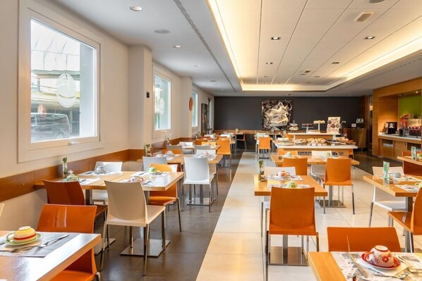 A spacious dining area with multiple tables and chairs, large windows, and a modern ceiling design. - Bes Hotel Bergamo West (Mozzo)