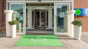 A hotel entrance with a revolving door, glass doors, and a green mat with a logo. - Bes Hotel Bergamo West (Mozzo)