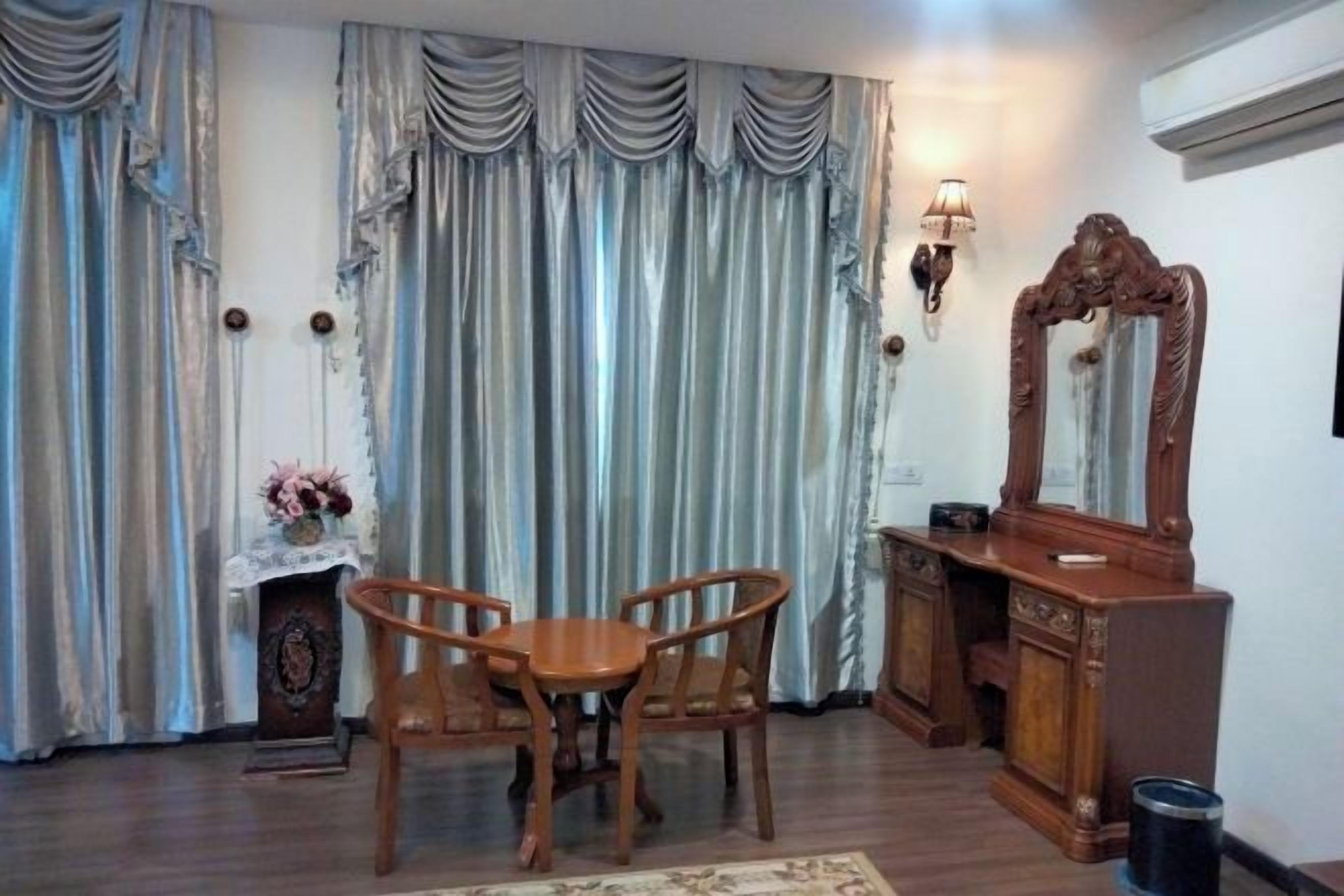 A room with a wooden dining table and chairs, a mirror, a fireplace with a lace cover, and curtains.