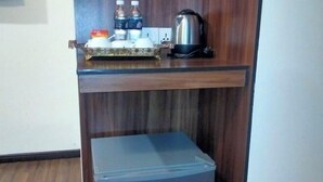 A kitchen with a small refrigerator, a kettle, and a shelf with bottles and a tray. - K GARDEN HOTEL PARIT BUNTAR (Parit Buntar)