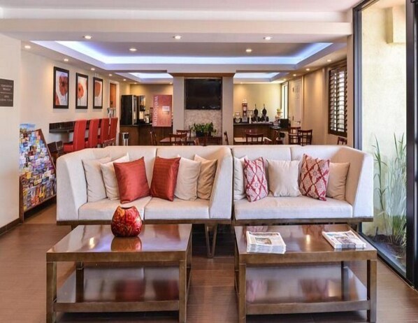 A modern hotel lobby with a large sofa, two coffee tables, and a reception area in the background. - The Cove Hotel, Ascend Hotel Collection (Long Beach)