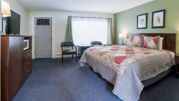 A hotel room with a bed, a desk, a chair, a television, and a door.