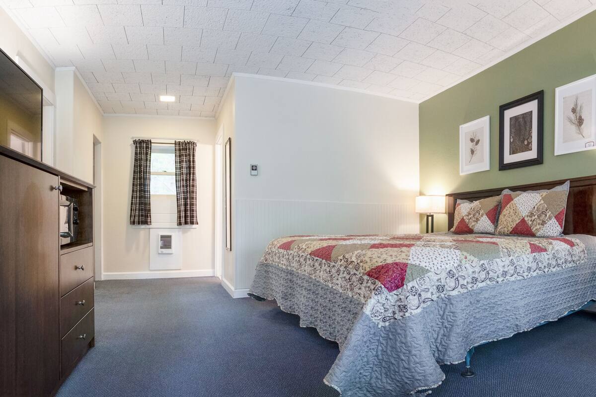 A bedroom with a large bed, a dresser, a nightstand, and a window with curtains.