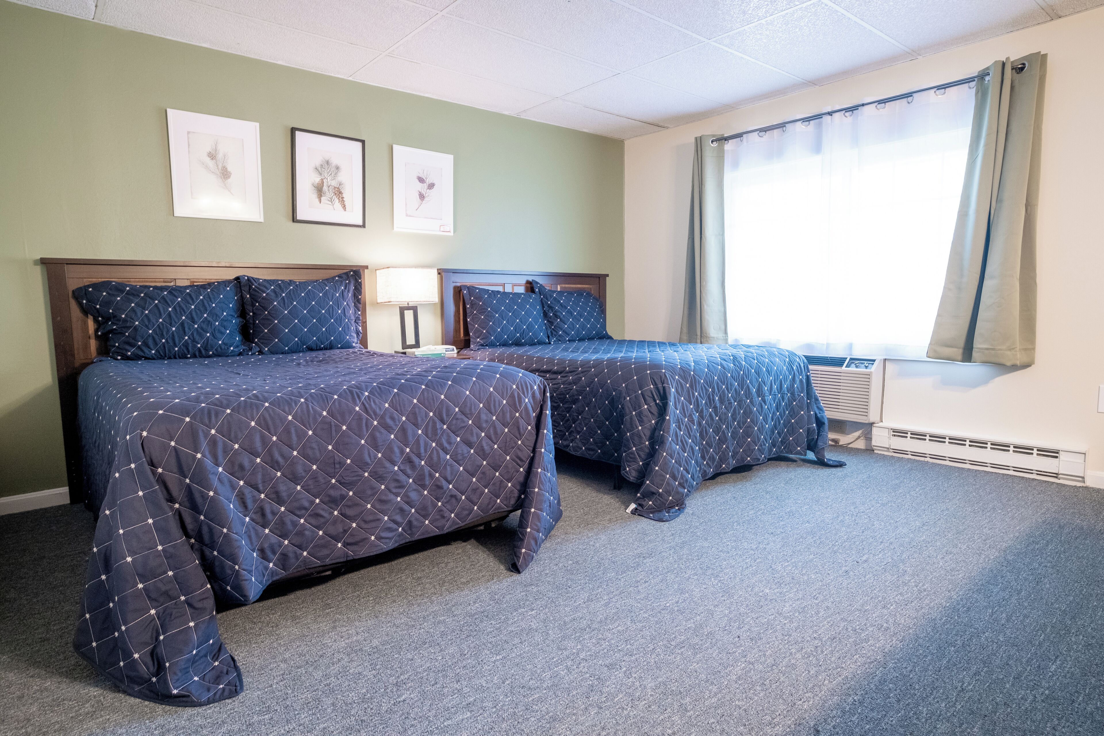 A hotel room with two beds, a window with curtains, and framed pictures on the wall.