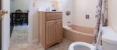 A bathroom with a toilet, bathtub, and sink. There is a vanity with a mirror and lights above the mirror. The floor is tiled, and there is a shower curtain with a floral pattern.