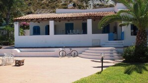 Un edificio bianco con tetto in tegole, una bicicletta parcheggiata davanti e una palma a destra.