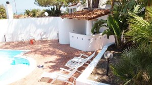 Area piscina con sedie a sdraio bianche, un piccolo angolo bar e un muro bianco decorato con piastrelle.