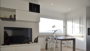 A modern kitchen with a flat-screen TV, white cabinets, a dining table with chairs, and a window with a view of the city. - Bougainvillier
Villa in Pedra Longa. Panoramic view, private pool. (Porto Istana)