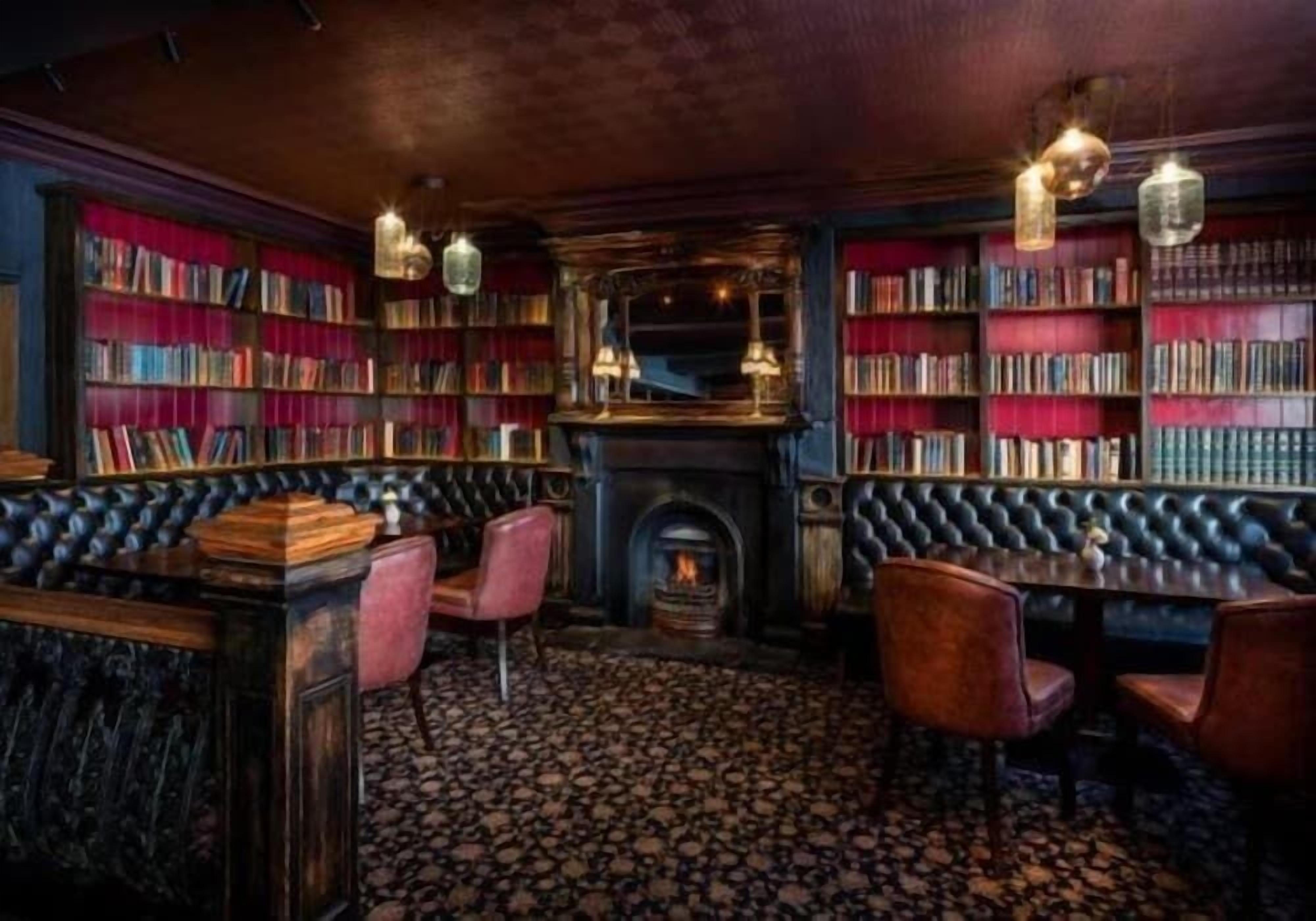 A cozy library with bookshelves, a fireplace, and leather seating.