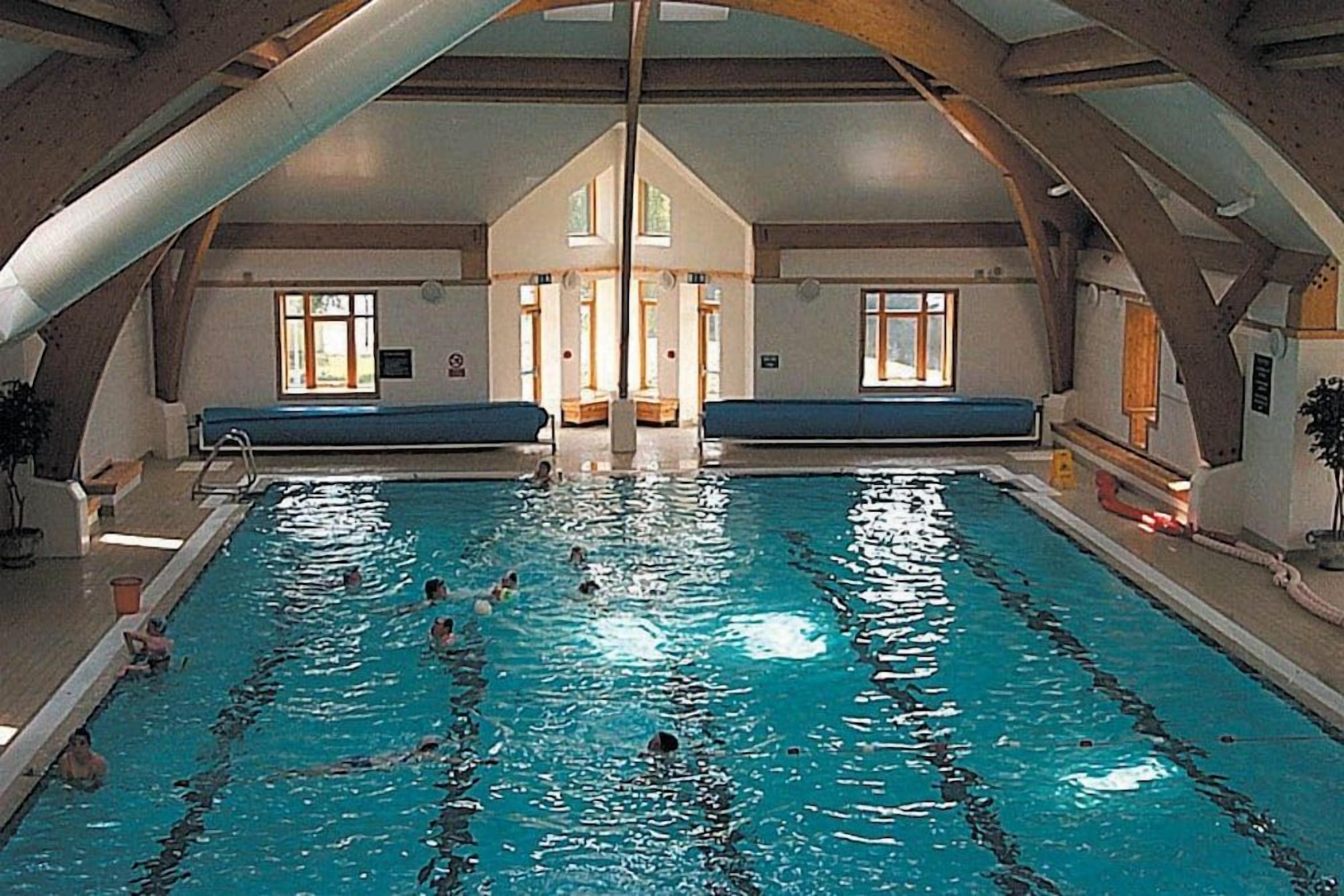 An indoor swimming pool with multiple lanes, benches along the sides, and a high arched ceiling.