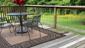 Une terrasse en bois avec une table et des chaises, entourée d’une clôture en métal et d’une végétation luxuriante.