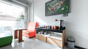 A modern kitchen with a black countertop, a coffee machine, and a kettle. There is a red chair and a green sofa. - The Cabin Hotel Sutomo (Yogyakarta)