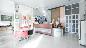 A hotel reception area with a counter, a seating area with a table and chairs, and a large screen displaying information. - The Cabin Hotel Sutomo (Yogyakarta)