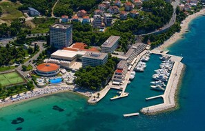 An aerial view of a coastal area with a marina, buildings, and a beach. - Spacious Sea View Villa with Basketball Court near Split! (Podstrana)