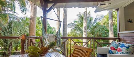 A wooden deck with a table and chairs, a hammock, and a sofa with patterned cushions.