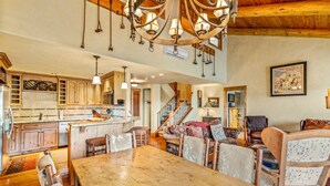 Un'ampia cucina con mobili in legno e un'isola grande, una zona pranzo con tavolo e sedie di legno, e un accogliente soggiorno con camino.