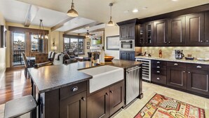 A spacious kitchen with dark wood cabinets, a large island with a sink, and a view of the city through large windows. - Edgemont 2507 Luxury On Mountain Condo With Ski-In/Ski-Out Access! (Steamboat Springs)