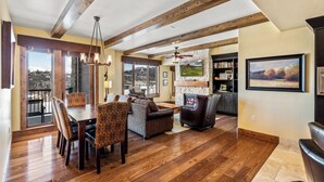 A spacious living room with wooden floors, a fireplace, a dining area with patterned chairs, and large windows offering a view of the city. - Edgemont 2507 Luxury On Mountain Condo With Ski-In/Ski-Out Access! (Steamboat Springs)