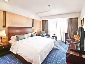 A hotel room with a large bed, a desk, a chair, a TV, and a window with curtains.