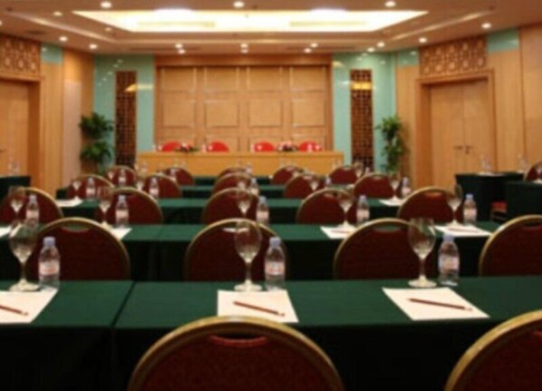 Een congreszaal met rijen tafels, stoelen en waterflesjes.