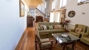 A cozy living room with a green sofa, wooden chairs, a glass coffee table, and a staircase leading to an upper level.
