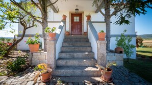 A stone staircase leading to a wooden door, flanked by potted plants and a clear view of the surrounding landscape.