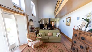 A spacious living room with a sofa, armchair, and wooden dresser. A large window allows natural light to fill the room.