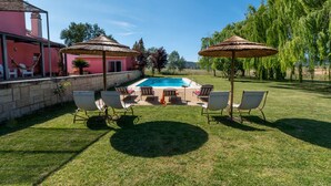 A pool area with lounge chairs and umbrellas, surrounded by a grassy lawn and trees.