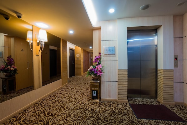 A hotel lobby with a patterned carpet, a reception desk, a wall-mounted elevator, and a security camera. - Jc Mark Hotel (Bintulu)