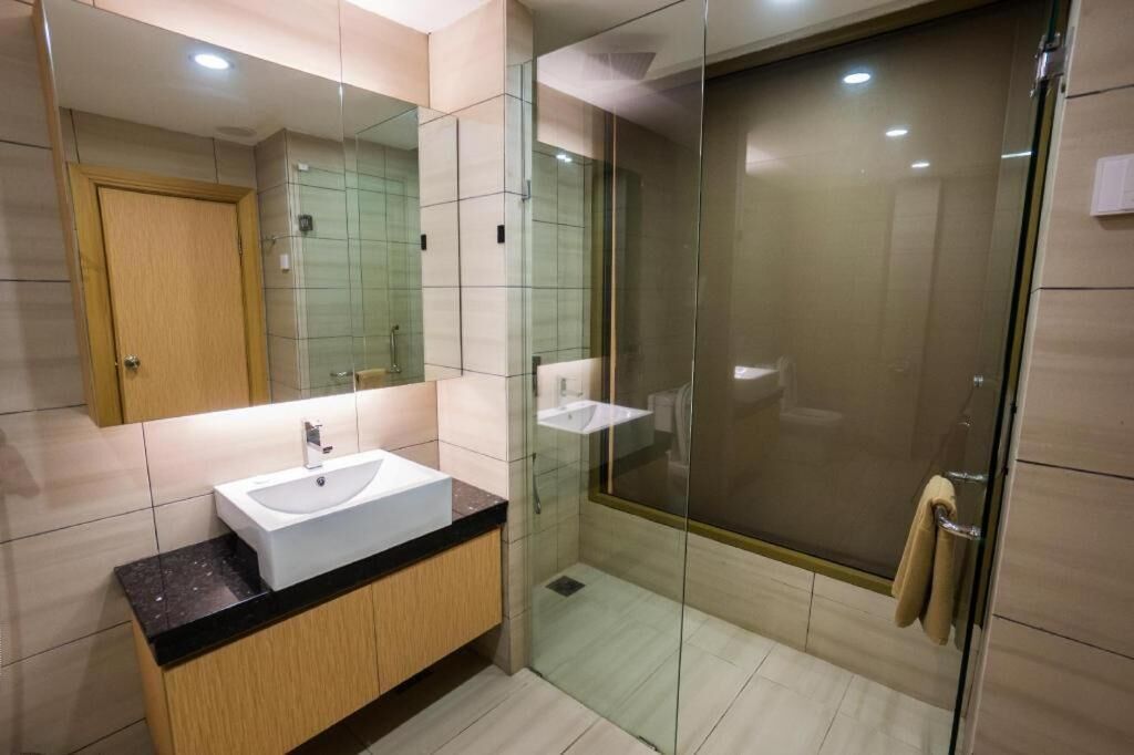 Un baño moderno con ducha envuelta en vidrio, un lavamanos blanco y un mueble de madera.