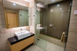 A modern bathroom with a glass-enclosed shower, a white sink, and a wooden cabinet. - Jc Mark Hotel (Bintulu)
