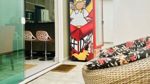 A modern living room with a large Simpsons-themed cabinet, a wicker sofa, and a glass sliding door leading to a kitchen. - Wonderful house ❤️   (São Sebastião)