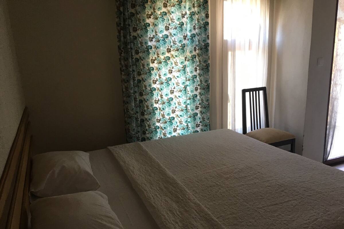 A bedroom with a bed, a chair, and a window with floral curtains.