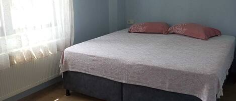 A bedroom with a bed, a window with sheer curtains, and a radiator.