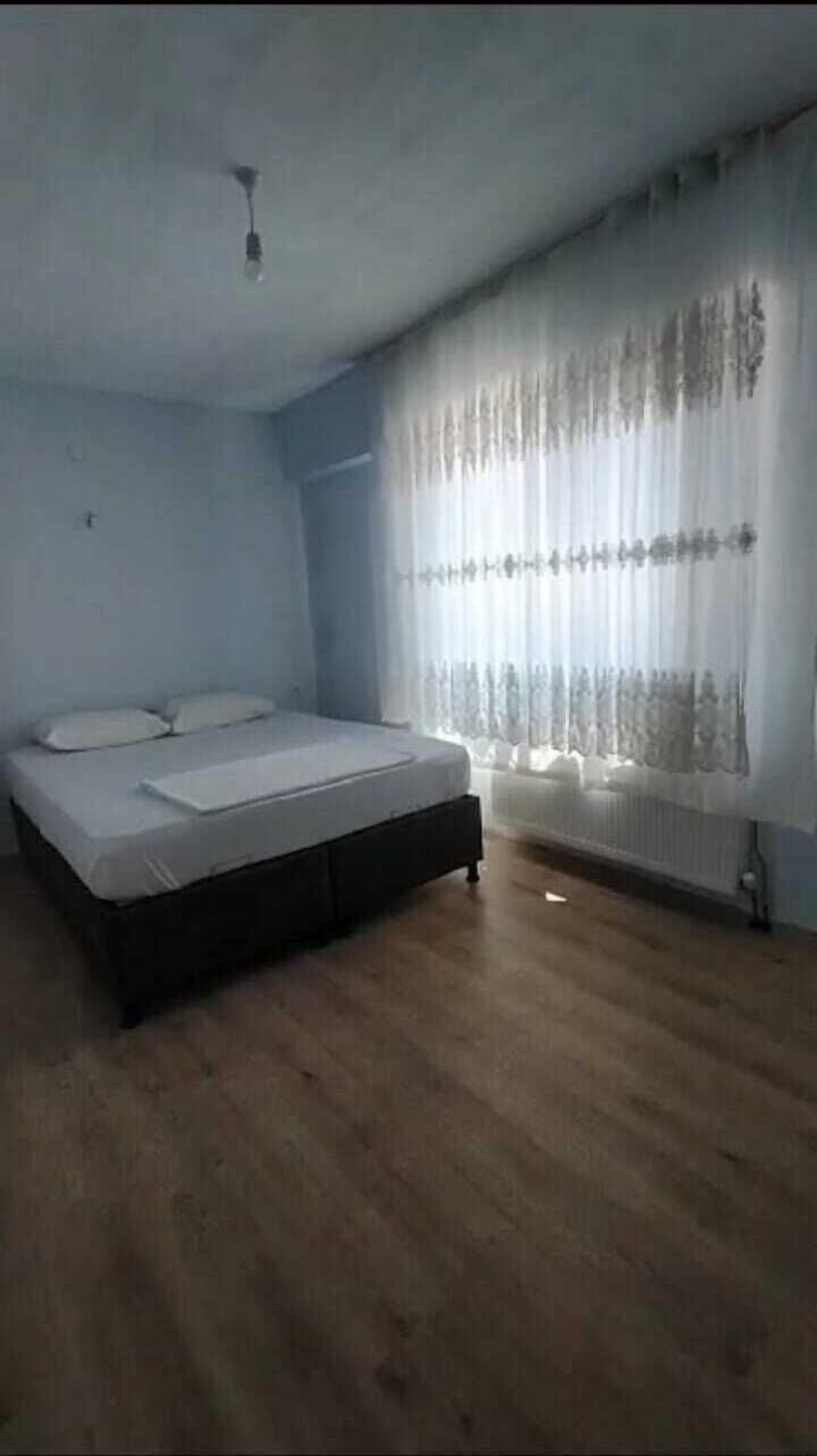 A bedroom with a bed, a radiator, and a window with curtains.