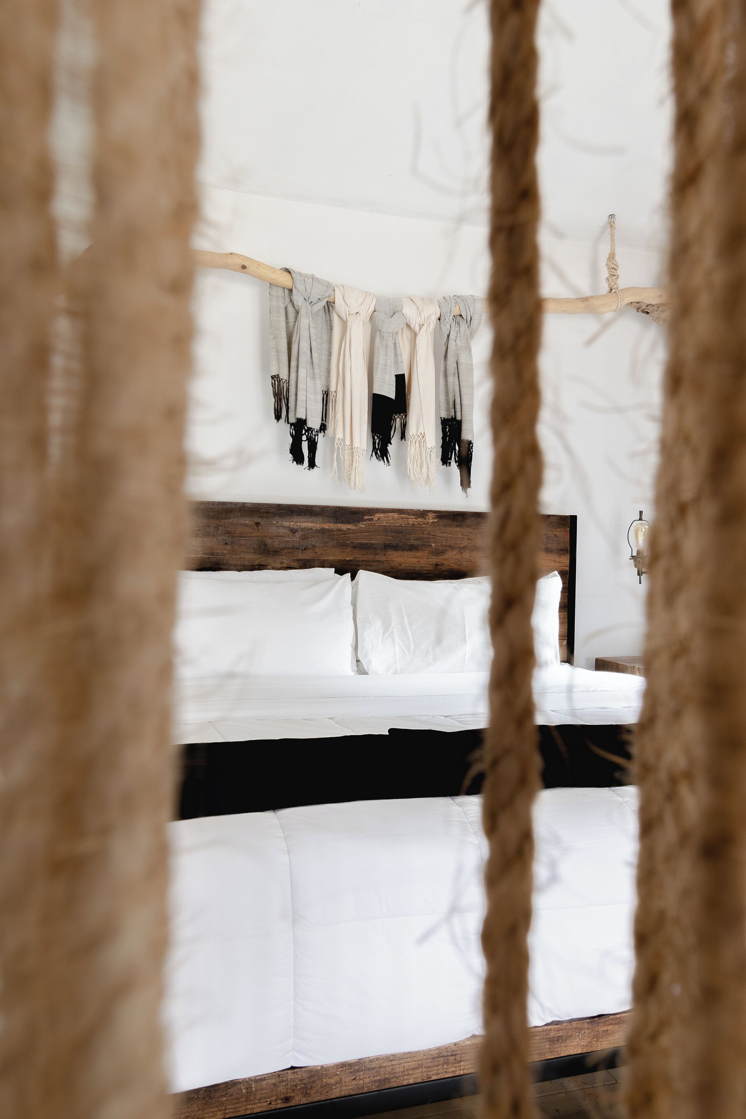 A bed with white linens and a wooden headboard, with ropes hanging on the wall above.