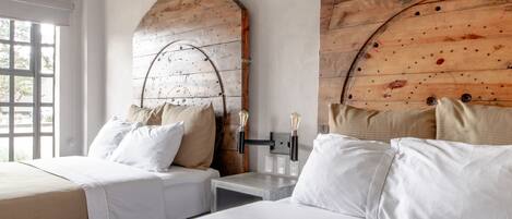 Habitación de hotel con dos camas, cabeceros de madera, un ventanal grande y un adorno colgante de ramas.