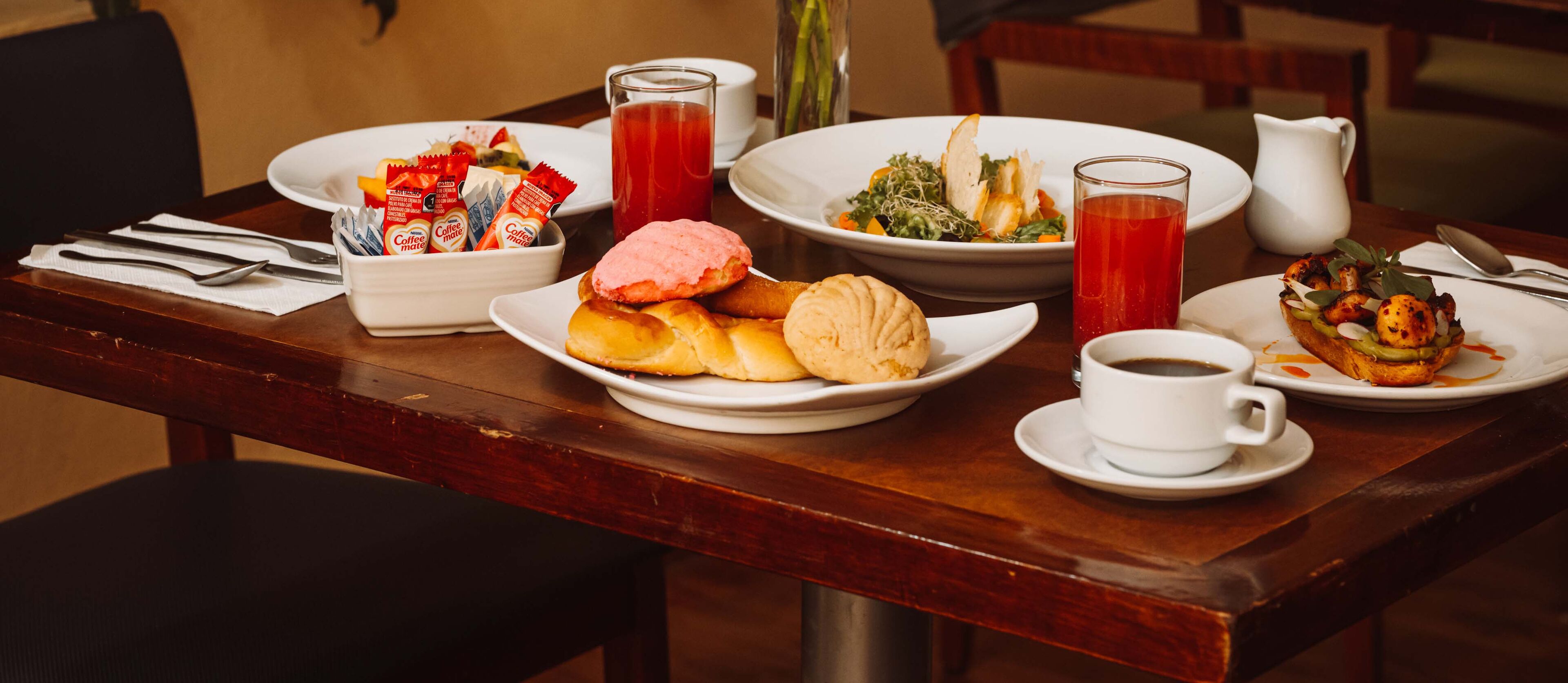 A dining table with breakfast items including pastries, a salad, coffee, and a pitcher of juice.