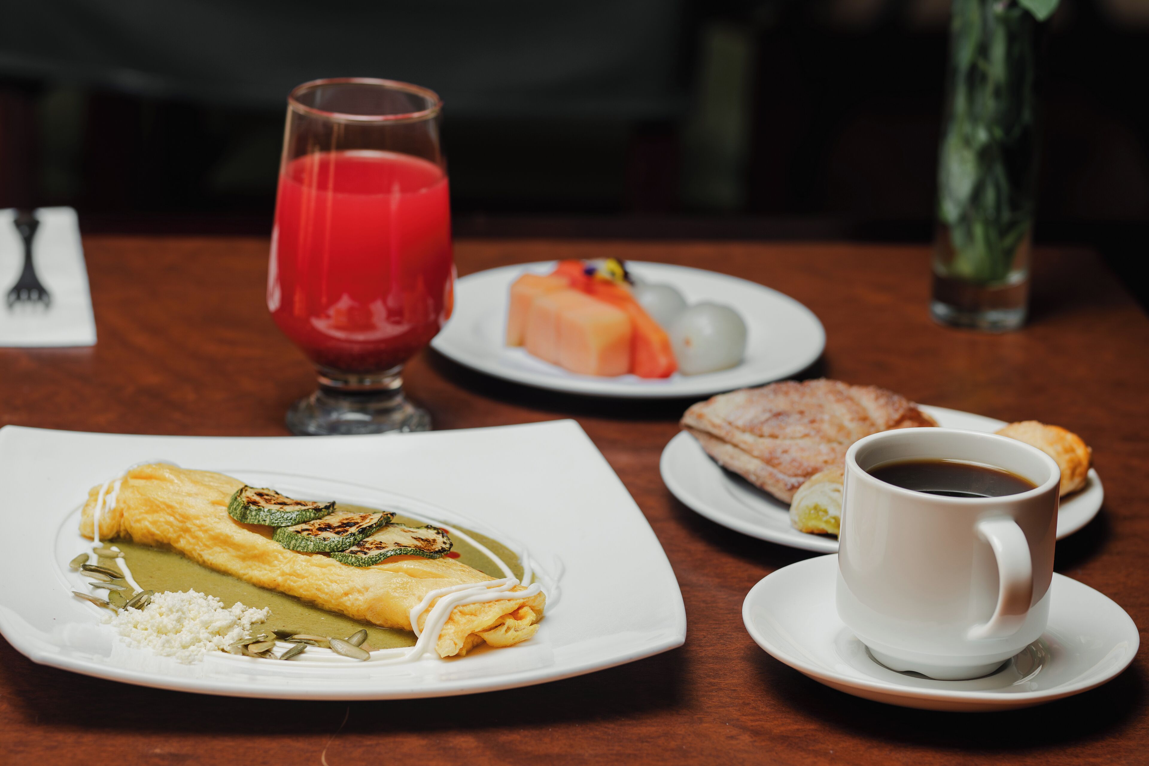 A table with a plate of food, a glass of red juice, a cup of coffee, and a vase with flowers.