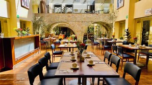 A spacious restaurant with multiple dining tables and chairs, a stone archway, and a variety of plants and flowers. - Hotel Rocaval (San Cristóbal de las Casas)