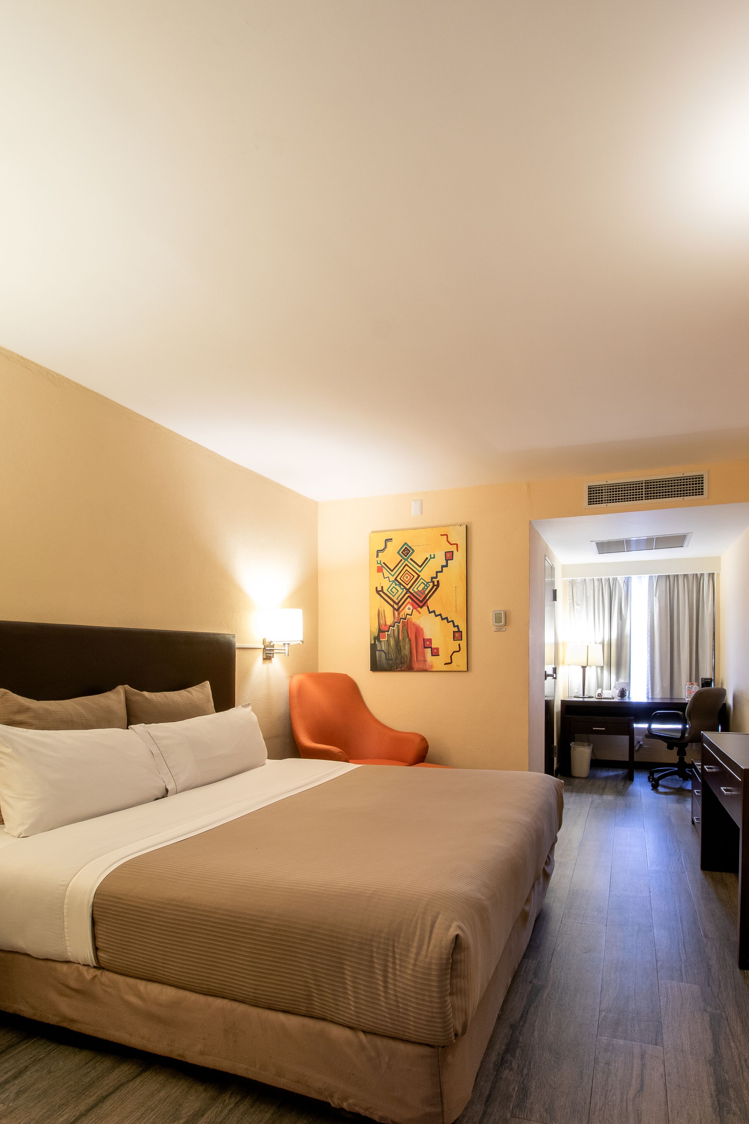 A hotel room with a bed, a desk, a chair, and a painting on the wall.