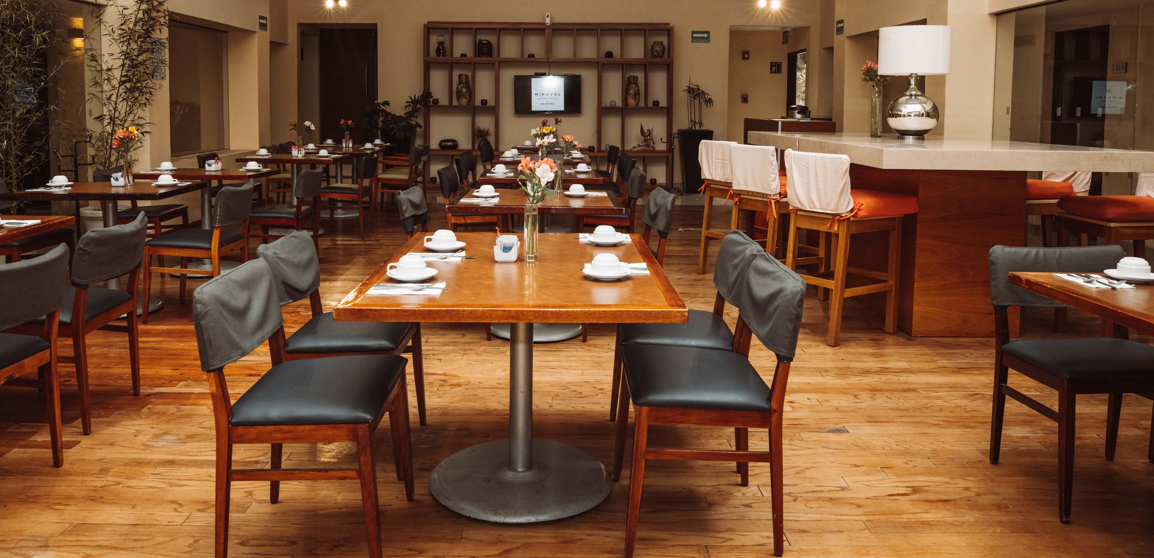 A restaurant with wooden tables and chairs, a TV mounted on the wall, and a counter with a lamp.