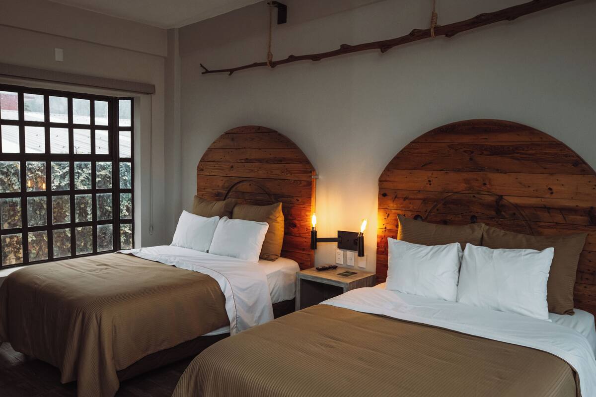 A room with two beds, wooden walls, and a large window.