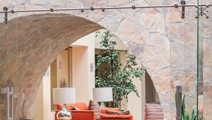 A lobby with a stone archway, seating area with orange couches, a wooden table, and a potted plant. - Hotel Rocaval (San Cristóbal de las Casas)