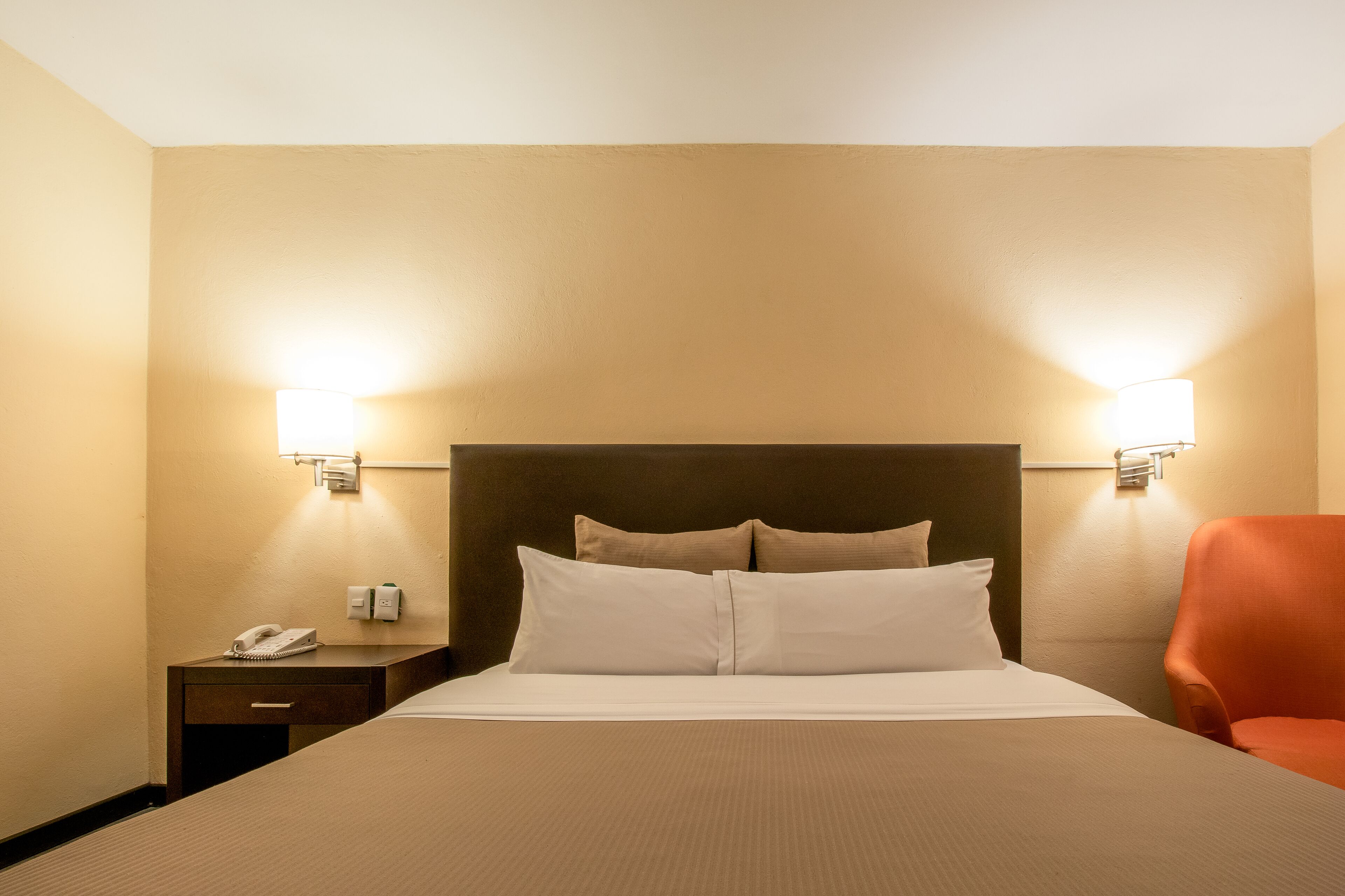A hotel room with a large bed, two bedside lamps, a nightstand with a phone, and a chair.