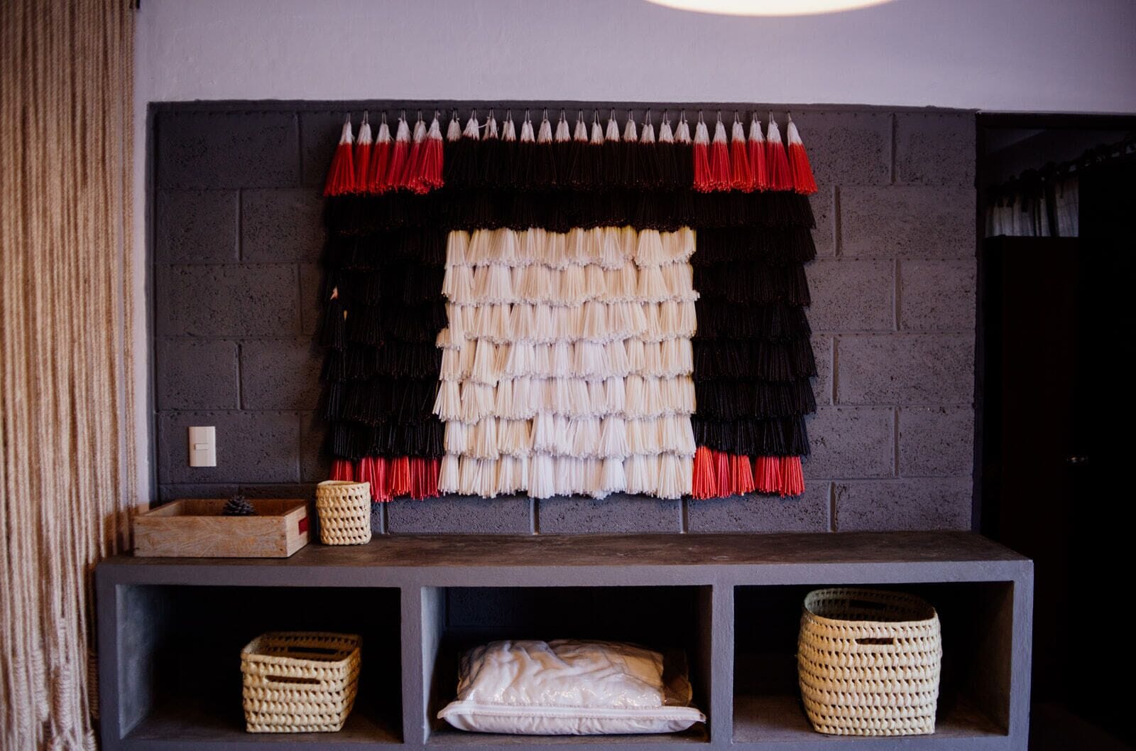 A fireplace with a decorative mantle featuring a black and white pattern, flanked by red tassels. Below, there are three woven baskets on shelves.